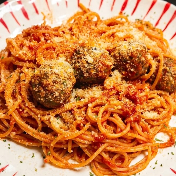 Spaghetti with meatballs and tomato sauce, topped with grated cheese and parsley on a striped plate.