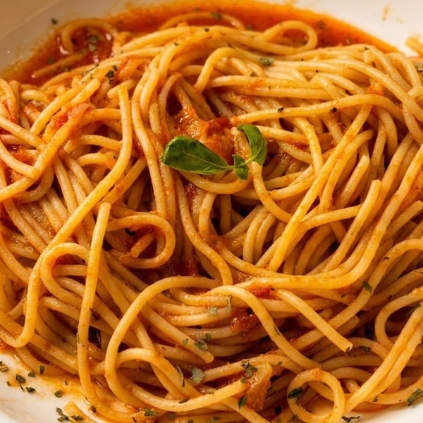 A white bowl filled with spaghetti in red sauce, garnished with a basil leaf and herbs.
